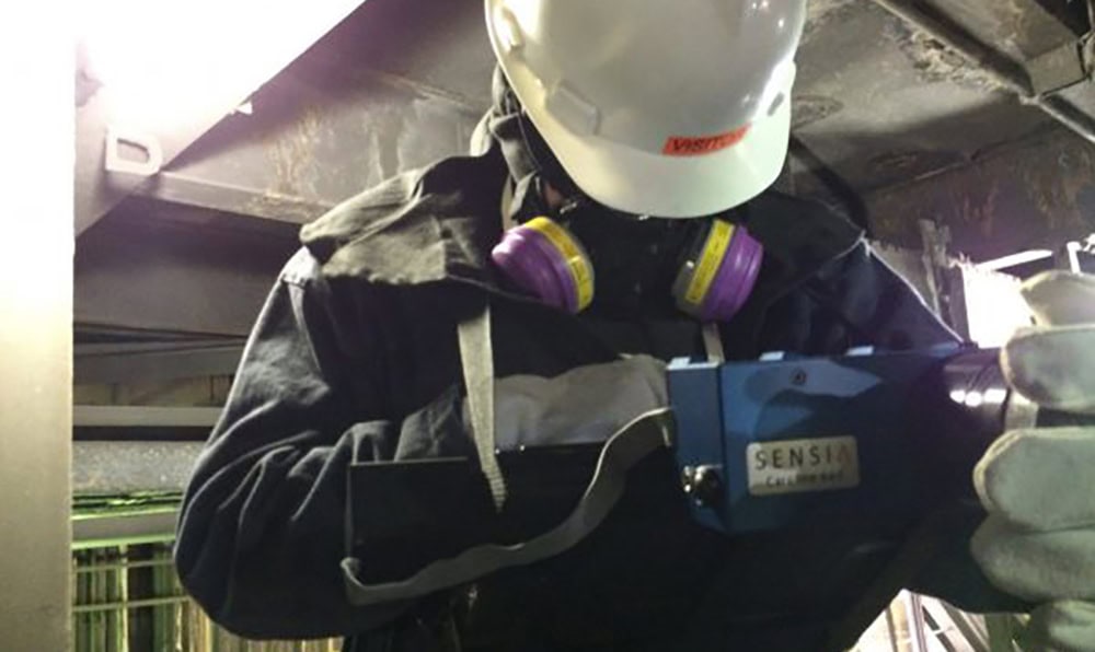 Worker using SENSIA device for SO2 leak detection in industrial setting.